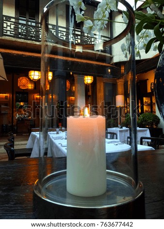 Circle glass jars with lit candle inside on dark wooden and dinner tables.