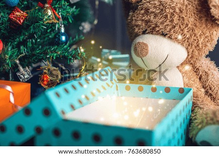 A Teddy bear opens a gift on background glowing Christmas tree. The concept of new year's eve Magic