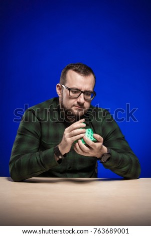 Emotional man in glasses holds in hands boxes with gifts, posing on blue background
