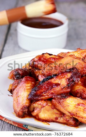 Plate of chicken wings with selective focus on chicken at the edge of plate and extreme shallow depth of field. BBQ sauce with basting brush in the background.