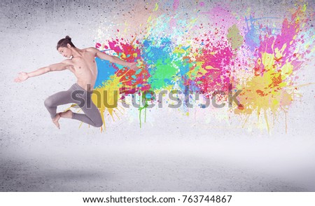 Modern street dancer jumping with colorful paint splashes on back wall concept