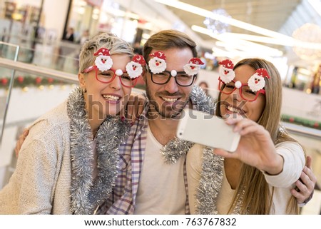 Friends with funny eyeglasses with Santa Claus making selfie in shopping mall
