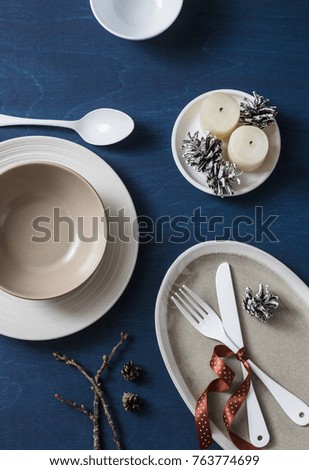 Christmas lunch food served table. Empty plates, bowls, fork, knife, spoon, christmas decorations, cones and candles on blue wooden background, top view. Flat lay, free space
