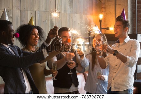 Happy multiracial people in party hats clown noses holding sparklers and champagne glasses celebrating New year eve together, excited diverse young friends having fun enjoying celebration together