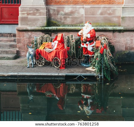 Statues of Santa Claus and his donkey with all the gifts near the Covered market of Colmar building with reflection in the Colmar Canal called Little Venice