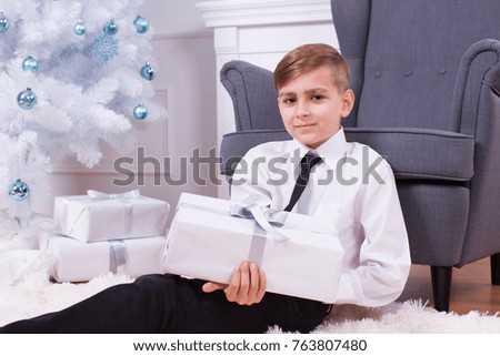 happy holidays, boy sitting and holding present near christmas tree
