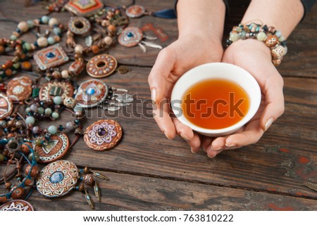 Hands with a tea bowl on a wooden table with clay ethnic decorations