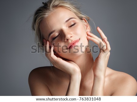 Young girl touching her face. Photo of blonde girl with perfect skin on grey background. Youth and Beauty