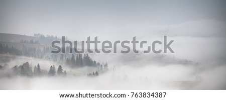 Panorama of forest covered by low clouds. Autumn rain and fog on the mountain hills. Misty fall woodland. Royalty-Free Stock Photo #763834387