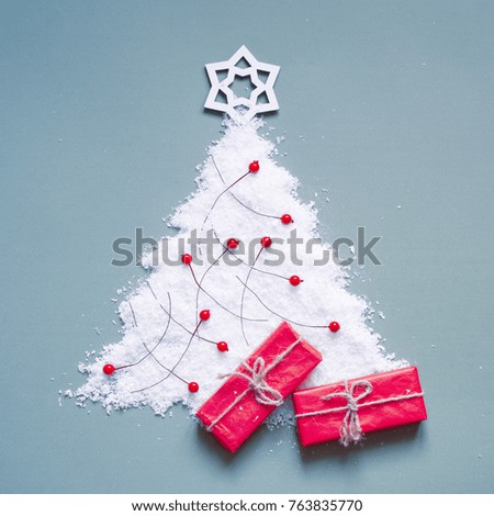 Christmas tree which is laid out from artificial snow, Christmas-tree decorations and red gift boxes on a blue background. Festive card