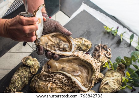 Oysters on the table. Chef opens the oysters. The restaurant's cuisine includes seafood, a knife, a glove, a lemon. Healthy fresh food. Royalty-Free Stock Photo #763842733