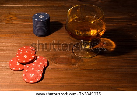 Poker chips and wine glass of cognac on wood table. Cognac drinks on wood background