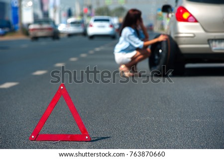 Emergency stop sign stands against the background of blurry young woman talking on the phone about help with car with broken wheel on the highway