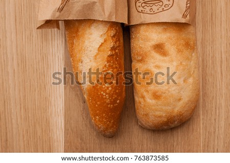 Two fresh baguettes, a French loaf and Italian ciabatta with a golden crust on a wooden background.