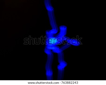 long exposure of blue sidewalk light forming an image of couple ice skating.  Man is holding woman with her leg in the air.