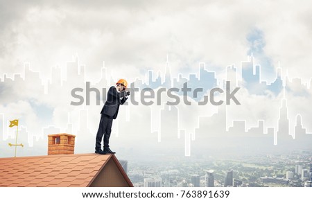 Young businessman in suit and helmet on roof edge in search of something new. Mixed media