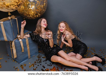 Cheerful european girl with blonde hair enjoying birthday party with friends. Indoor photo of refined female model with bright make-up lying on confetti beside gifts and laughing.