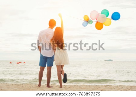 Romantic couple relaxing on the beach and enjoying beautiful sea view with colored balloons