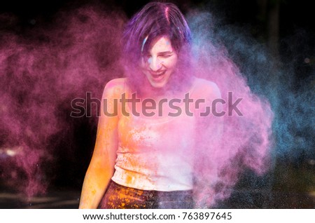 Emotional young woman posing with blowing Holi powder at the park