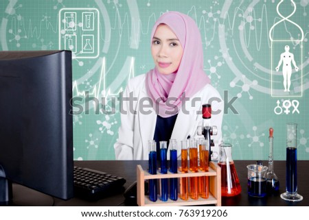 Image of female Muslim doctor smiling at the camera while sitting with green virtual screen background