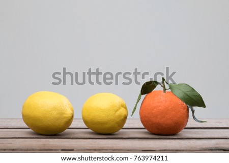 Still life of two lemons and one tangeringe with leafs. Arranged on a wooden floor, set up in a row. Photo is in a horizontal angle.
