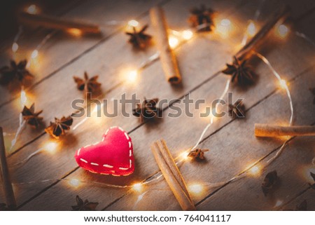 Holidays illuminations and heart shape toy with cinnamon and star anise around on wooden background. Image in old color style