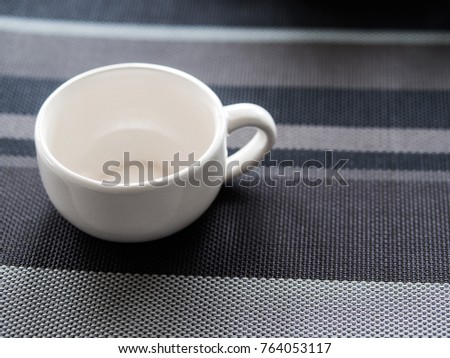 A white ceramic cup without coffee on the dark tone of tablecloth, picture with free copy space.