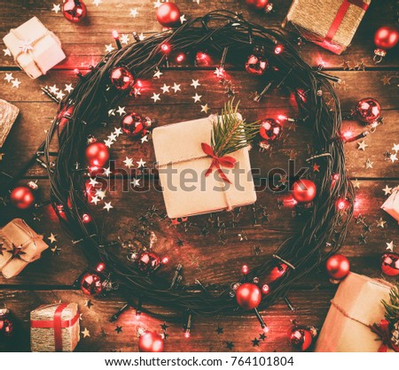 Wooden background with red lights and stars, surrounded by gifts and toys, in square shape, with effect. In the center is white, for the holiday message. Top view.