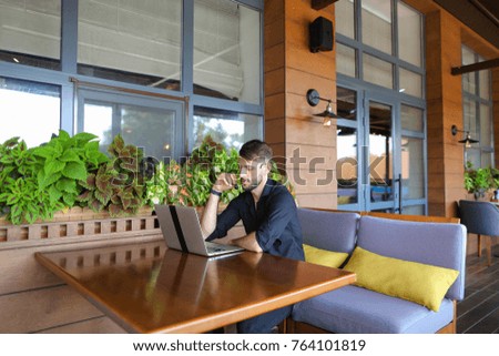 Internet consultant speaking to user with video call and headset microphone. Assured handsome male person dressed in black shirt sitting near green indoor plants. Concept of practical experience and