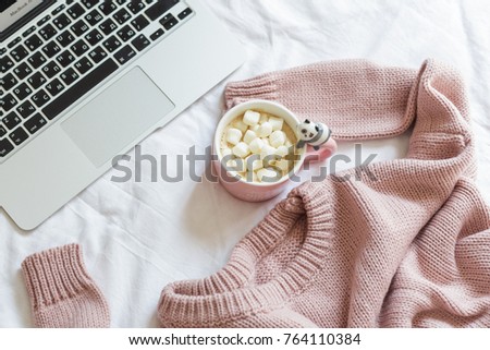pink knitted sweater, a cup of coffee with marshmallows and a notebook lie on the bed in the bedroom