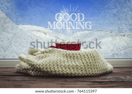 A beautiful image of a red cup and a white scarf on a window sill with a beautiful winter landscape outside the window.