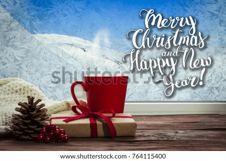 A beautiful image of a red cup and gift on a window sill with a beautiful winter landscape outside the window. Added text.