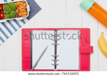 Office desk with supplies and lunch box with vegetables and almond. Top view with space for your text