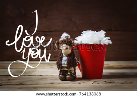 White rose flower in a red cup and toy on a wooden background. Inscription I love you.