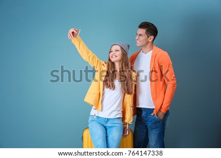 Happy tourists taking selfie on color background