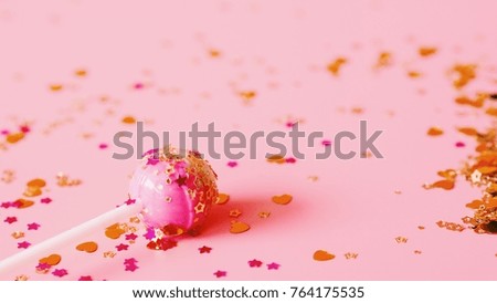Close up lollipop with golden glitter on pink background.