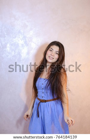 Cute young woman smiles beautifully and in high spirits looks and poses, changing poses to camera in bright silvery confetti, standing against background of light wall in room. Dark-haired woman