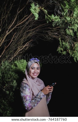 Portrait of beautiful  young asian muslim woman posing with mobile phone over dark background
