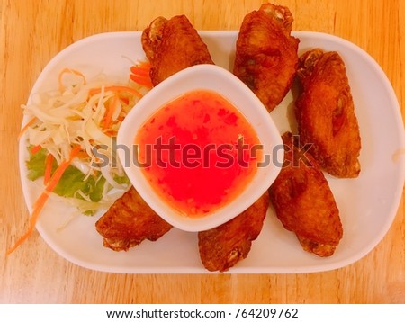 Fried chicken wings with chicken sauce and vegetable on white plate, place on brown wood table. Concept be used for present about restaurant business. Blur and exposure picture.