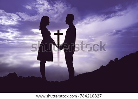 Portrait of romantic couple holding hands and looking at each other with christian cross against dramatic sky background