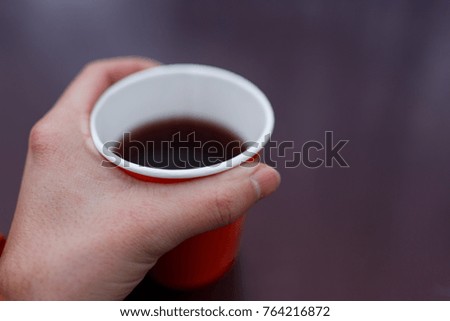 Picture of man's hand holding red paper glass with tea