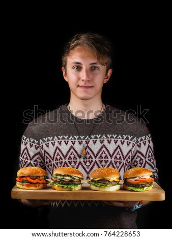 young guy holding a burgers on a wooden tray. black background.
