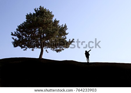 A silhouette of a woman pointing away from a single tree in a field. Daegu, South Korea