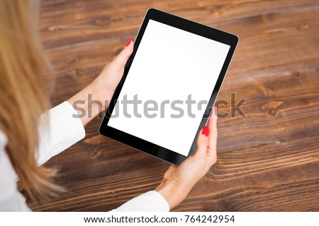 Woman holding tablet on wooden table.