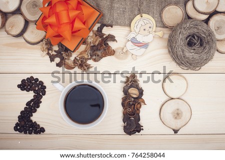 2018 inscription of coffee beans, cup, dry flowers and wooden slices, an orange gift box with an orange bow, a toy angel and a skein of threads, light wooden background, top view