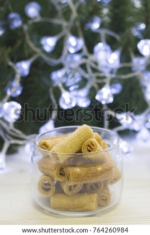 A glass clear bowl of fresh crispy cookies against a Christmas tree with white fairy lights, light background