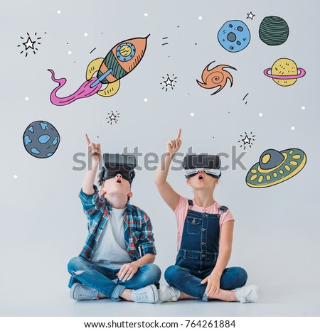 casual children using virtual reality headsets while sitting on the floor with doodle space pictures on walls