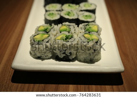 Sushi rolls lit dramatically on a white plate on a wooden table.