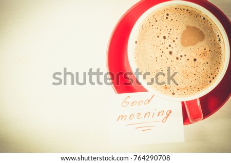 A Red Cup of Cappuccino and Notes Good Morning on Light Rustic Table From Above. Toned Image. Selective Focus.