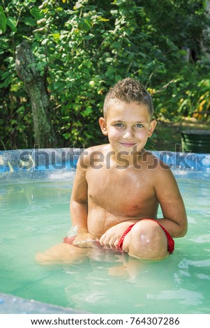 In the summer in the courtyard near the bushes in the pool is a small handsome wet boy.